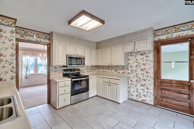 kitchen featuring an inviting chandelier, light countertops, baseboards, wallpapered walls, and appliances with stainless steel finishes