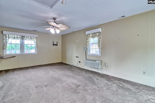 unfurnished room with carpet flooring, ceiling fan, visible vents, an AC wall unit, and a textured ceiling