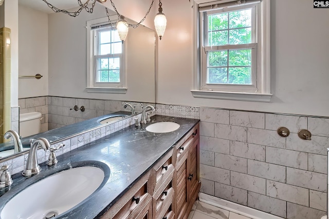 full bathroom featuring tile walls, toilet, wainscoting, and a sink