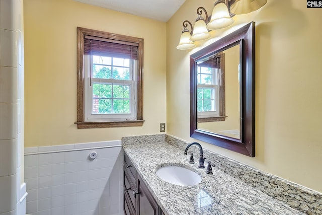 bathroom with tile walls, wainscoting, vanity, and plenty of natural light