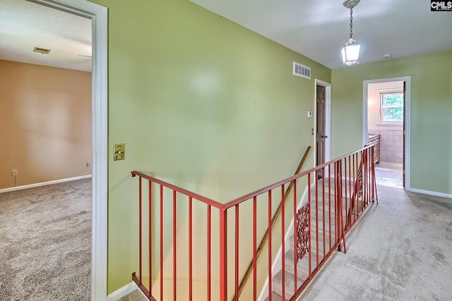 corridor featuring an upstairs landing, visible vents, and carpet floors