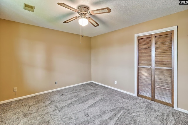 carpeted empty room featuring a textured ceiling, ceiling fan, visible vents, and baseboards