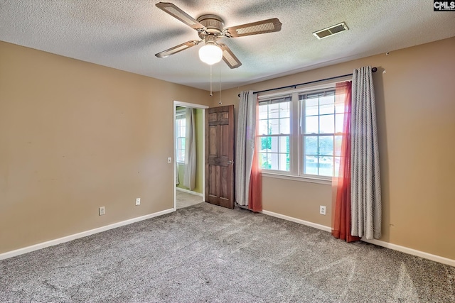 unfurnished room featuring a textured ceiling, carpet flooring, visible vents, baseboards, and a ceiling fan