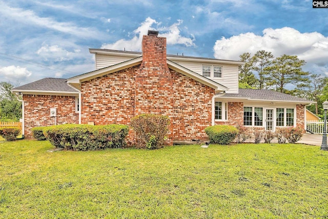 back of property featuring brick siding, roof with shingles, a yard, and a chimney