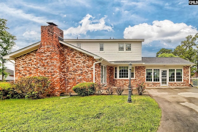 exterior space with driveway, a chimney, roof with shingles, a lawn, and brick siding