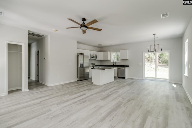 unfurnished living room with light wood-style flooring, a sink, visible vents, baseboards, and ceiling fan with notable chandelier