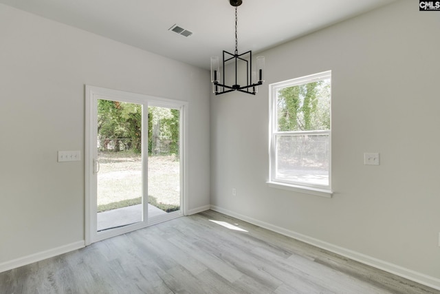 unfurnished dining area with visible vents, wood finished floors, a healthy amount of sunlight, and a chandelier
