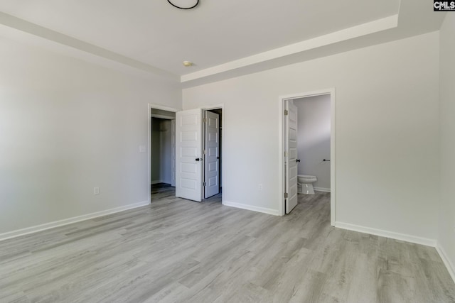 unfurnished bedroom with a closet, light wood-type flooring, a walk in closet, baseboards, and ensuite bathroom