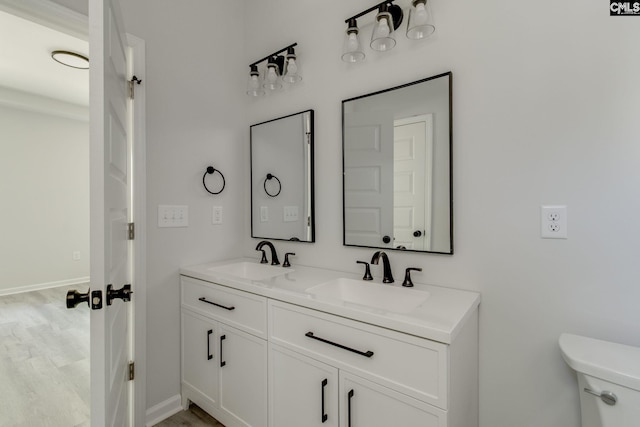 bathroom featuring toilet, double vanity, a sink, and baseboards