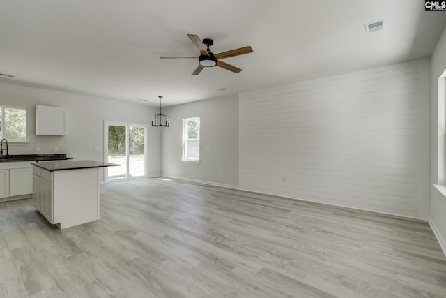 interior space featuring white cabinets, dark countertops, light wood-style flooring, and ceiling fan with notable chandelier
