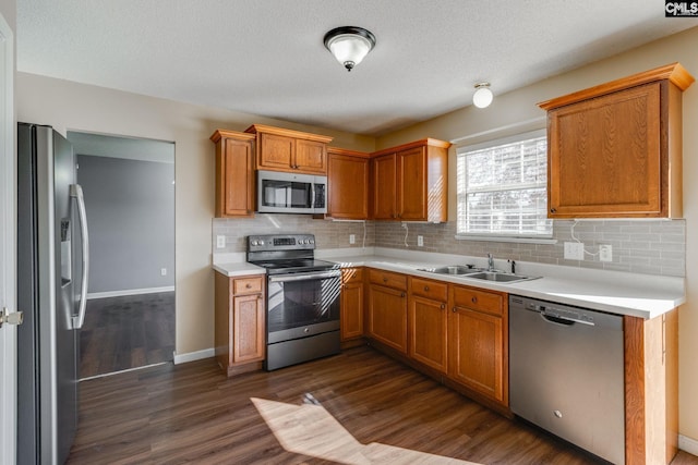 kitchen with stainless steel appliances, light countertops, backsplash, a sink, and dark wood-type flooring