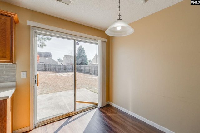 unfurnished dining area featuring a textured ceiling, baseboards, and dark wood finished floors