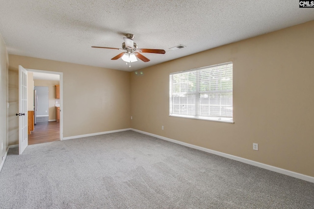 carpeted empty room with a textured ceiling, visible vents, a ceiling fan, and baseboards
