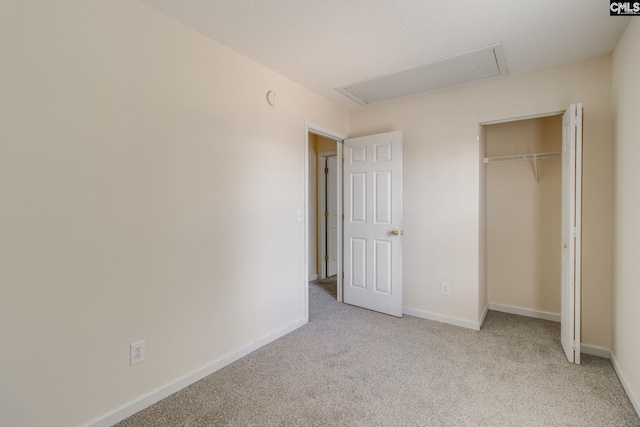 unfurnished bedroom featuring attic access, a closet, light colored carpet, and baseboards