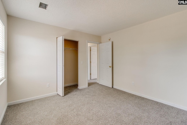 unfurnished bedroom featuring a textured ceiling, a closet, light carpet, and baseboards