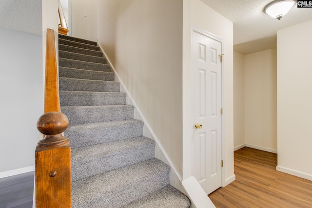 staircase featuring baseboards, wood finished floors, and a textured ceiling