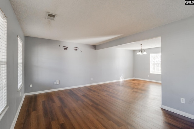 unfurnished room featuring a textured ceiling, visible vents, baseboards, an inviting chandelier, and wood finished floors