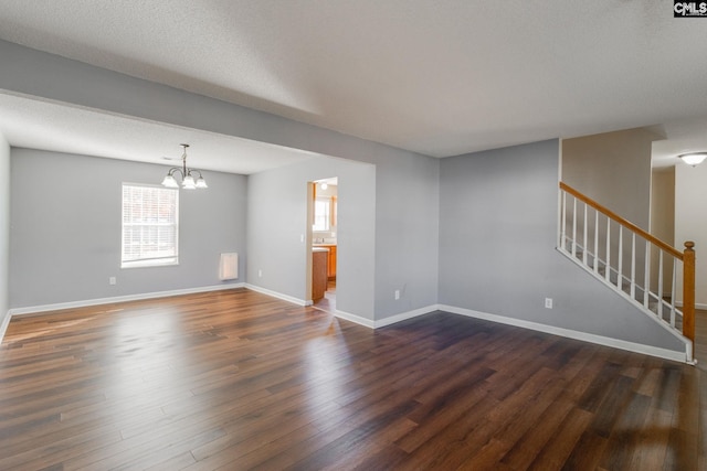 spare room with stairs, a notable chandelier, baseboards, and dark wood-type flooring
