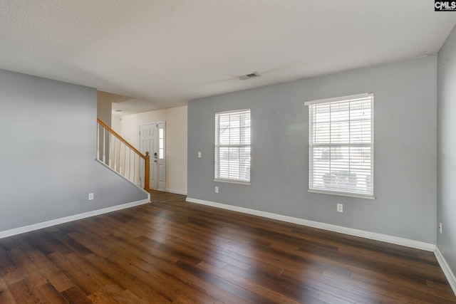 unfurnished room with dark wood finished floors, visible vents, stairs, and baseboards