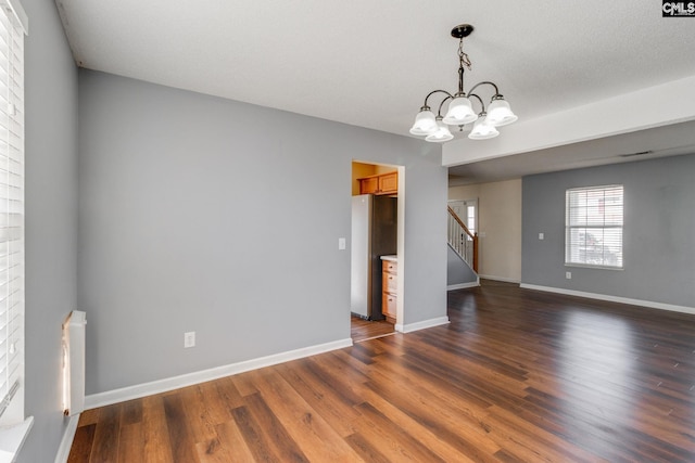 spare room with an inviting chandelier, stairway, dark wood finished floors, and baseboards