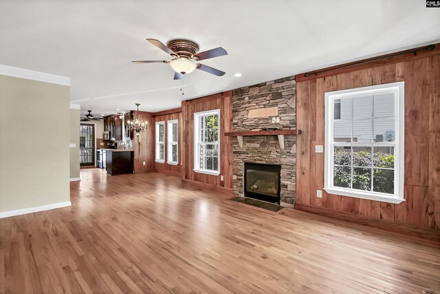 unfurnished living room with wood walls, a fireplace, baseboards, light wood-type flooring, and ceiling fan with notable chandelier