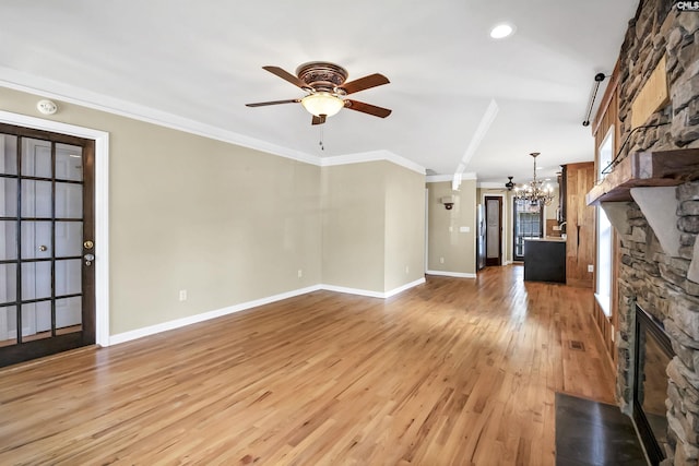 unfurnished living room with ornamental molding, a stone fireplace, light wood-style floors, baseboards, and ceiling fan with notable chandelier