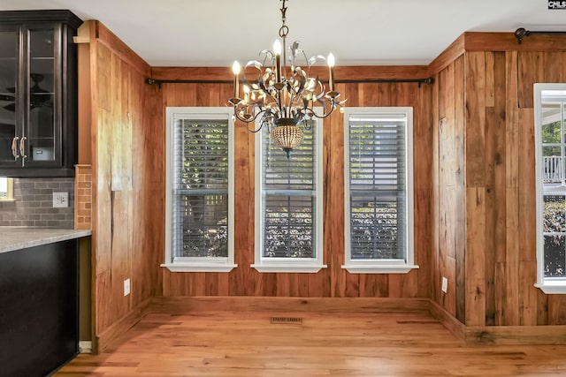 unfurnished dining area featuring wooden walls, baseboards, an inviting chandelier, and light wood-style floors