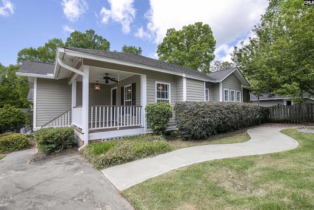 ranch-style home featuring a porch, a ceiling fan, a front yard, fence, and a shingled roof