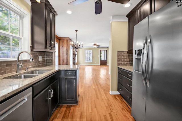 kitchen featuring ceiling fan with notable chandelier, tasteful backsplash, a sink, light wood finished floors, and appliances with stainless steel finishes