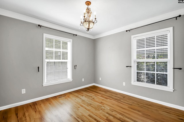 empty room featuring crown molding, an inviting chandelier, baseboards, wood finished floors, and visible vents
