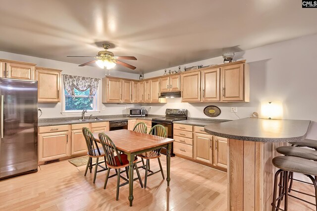 kitchen with light wood-style flooring, a breakfast bar area, light brown cabinetry, and black appliances