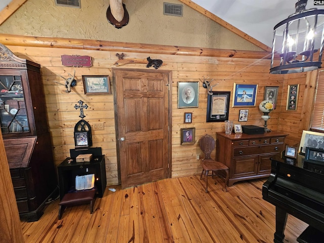 office space featuring visible vents, light wood-style flooring, lofted ceiling, and wooden walls