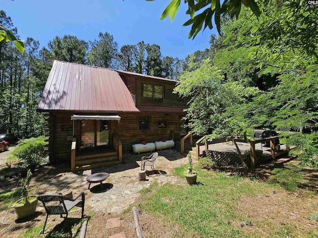 rear view of property with log siding, a fire pit, and a patio area