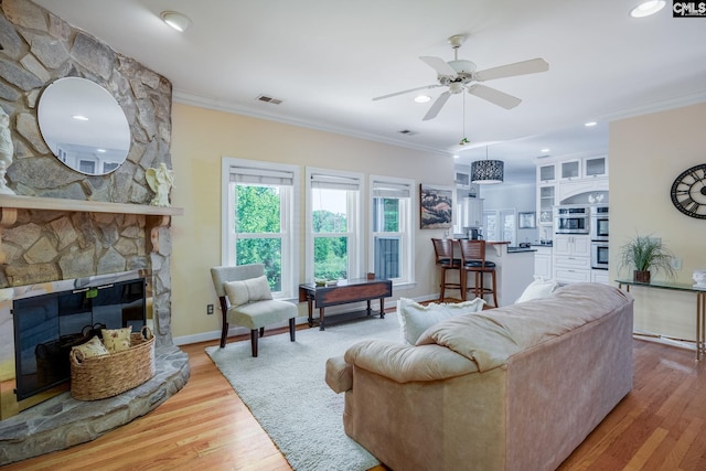 living area featuring baseboards, ceiling fan, light wood-style flooring, and crown molding