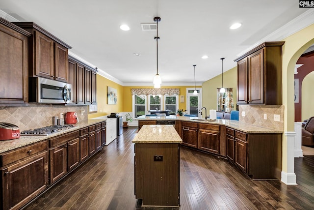 kitchen with backsplash, arched walkways, a sink, a peninsula, and stainless steel appliances