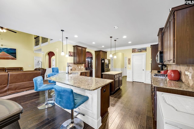 kitchen featuring a sink, a kitchen island, open floor plan, stainless steel microwave, and arched walkways
