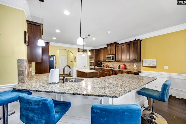 kitchen featuring appliances with stainless steel finishes, a sink, arched walkways, a center island, and ornamental molding