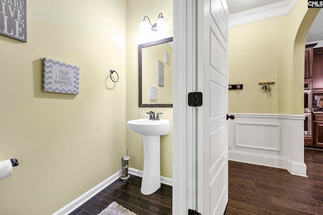 bathroom featuring crown molding, wainscoting, wood finished floors, baseboards, and a sink