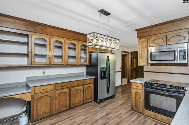kitchen featuring wood finished floors, glass insert cabinets, light countertops, appliances with stainless steel finishes, and decorative light fixtures