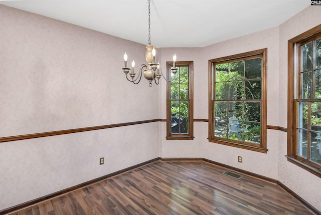 empty room featuring dark wood-style flooring, a chandelier, baseboards, and visible vents