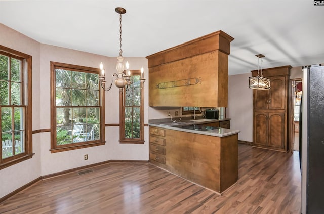 kitchen with an inviting chandelier, a peninsula, brown cabinets, and dark wood-style floors