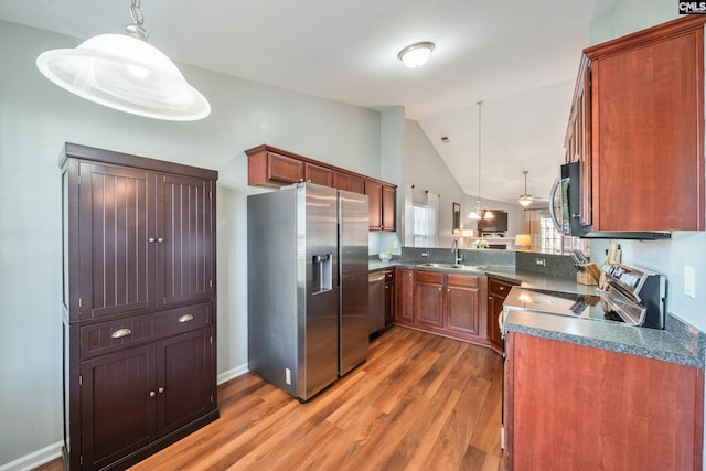 kitchen featuring dark countertops, a sink, light wood-style flooring, appliances with stainless steel finishes, and vaulted ceiling