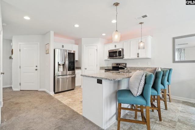 kitchen with appliances with stainless steel finishes, light stone counters, a peninsula, white cabinetry, and visible vents