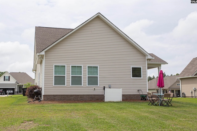 rear view of property featuring a lawn and roof with shingles