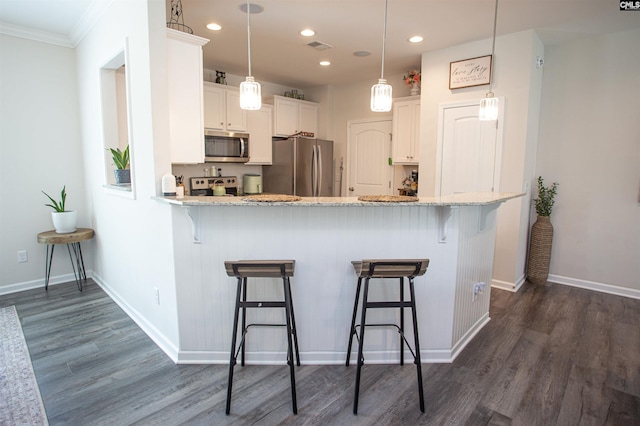 kitchen featuring dark wood-type flooring, appliances with stainless steel finishes, white cabinets, and a kitchen bar