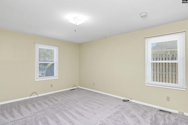 spare room featuring a textured ceiling, baseboards, visible vents, and carpet