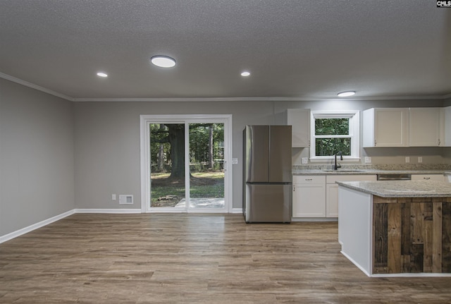 kitchen with crown molding, appliances with stainless steel finishes, wood finished floors, a sink, and white cabinetry