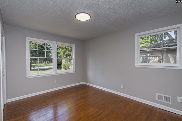 spare room featuring baseboards, a wealth of natural light, dark wood finished floors, and visible vents