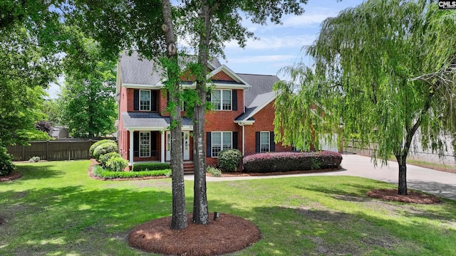 view of front of home with brick siding, fence, driveway, and a front yard