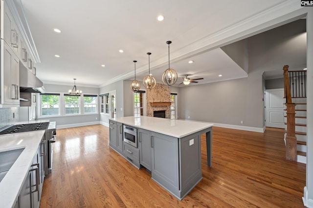 kitchen with built in microwave, a brick fireplace, gray cabinetry, ceiling fan with notable chandelier, and open floor plan